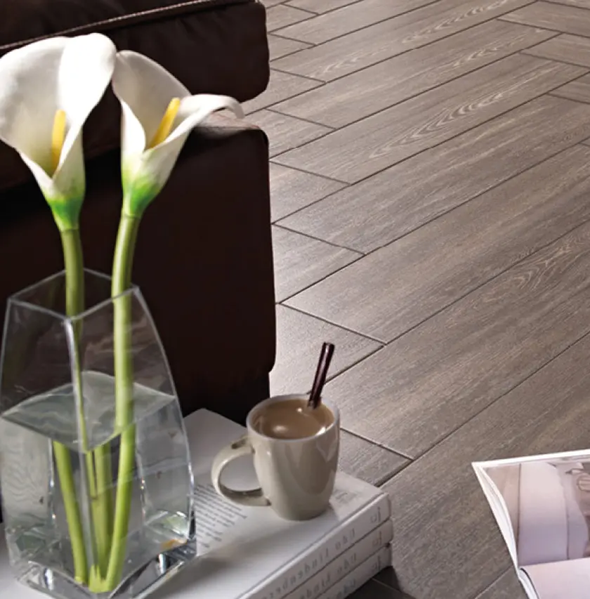 Detailaufnahme eines modernen Wohnzimmers mit dunklem Designboden in Holzoptik, Vase mit Calla-Blumen und Kaffeetasse auf Büchern, stilvolle Wohnaccessoires für gemütliches Ambiente.